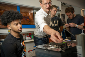 Surrounded by 3 students inside a lab, Kolle, center, reaches for an object