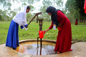 Two female students collect clean water from a tube well in a jug in Bangladesh. Photo credit: HM Shahidul Islam | Shutterstock.com