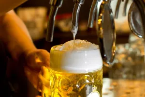 A glass of beer being filled from a tap, with a thick, foamy head on top.
