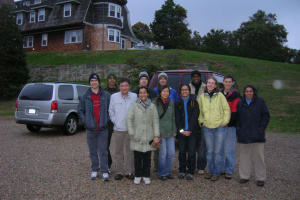 A group of people in front of a large house and a parked van.