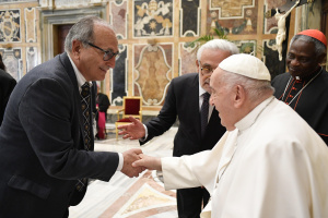 Kenneth Strzepek, in a suit and tie, shakes the hand of Pope Francis, with two other men in the background, in the Vatican