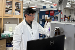 A person wearing a lab coat and goggles, looking at their work