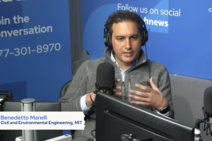 Benedetto Marelli wears a headset and sits in front of a large microphone in a radio show setting