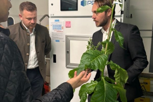 Robbie Wison holds a plant, showing it to two other people in a lab
