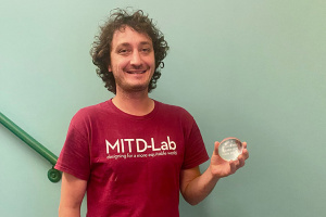Sweeney holding Infinite Mile award, smiling in red shirt