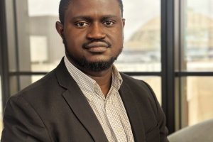 headshot of adeposi adeogun in a suit in front of a window
