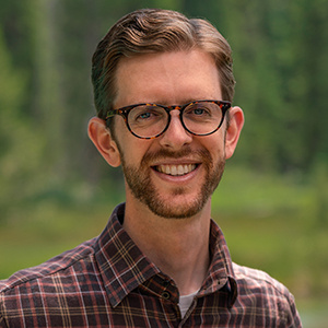 Headshot of Scott Odell, man with glasses and a red plaid shirt standing outside smiling