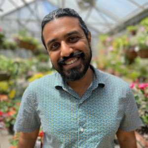 Gokul Sampath, standing inside a green house, with a dark beard 