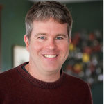 Headshot of David Des Marais smiling in a red sweater