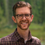 Headshot of Scott Odell, man with glasses and a red plaid shirt standing outside smiling