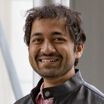 Devashish Gokhale looking at the camera smiling, with dark hair and a black leather jacket
