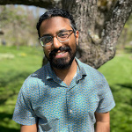 Gokul Sampath, standing outside in front of a tree with dark beard and glasses
