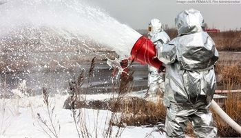 Two people in silver hazmat suits spraying a foam solution into a body of water
