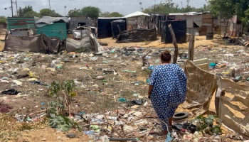 A woman standing near a group of make shift shelters at the La-Pista settlement