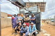 Team of people standing outside a shipping container in a dirt area outside