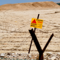 Dry, arid land with a bright yellow and red sign in the middle saying "danger mines"