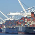 Large cargo ships being loaded with shipping containers by cranes from the dock. 