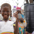 Ghanaian girl holds two water bottles: One filled with sediment and the other clean.