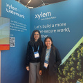 2026 travel grantees Priyanka and Hao in front of blue Xylem poster
