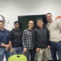Group of people making up the Nona team stand in a line in front of a TV mounted on a wall