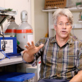 Professor Charlie Harvey, mid sentence, in his lab with equipment and a computer in the background