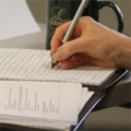 a light skinned hand holding a pen writing in a notebook